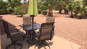 Una terrazza esterna con un tavolo e quattro sedie, circondata da ghiaia e palme.