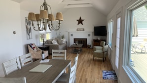 Un salon spacieux avec une cheminée, un coin repas avec une table en bois et une grande fenêtre donnant sur l’extérieur.