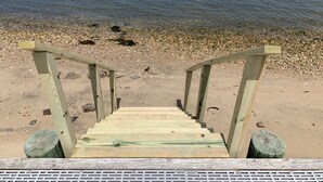 Un escalier en bois mène à une plage de galets, bordée par une mer calme.