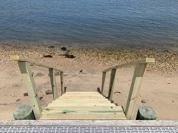 Stairs lead down to a pebble beach with clear water in the background.
