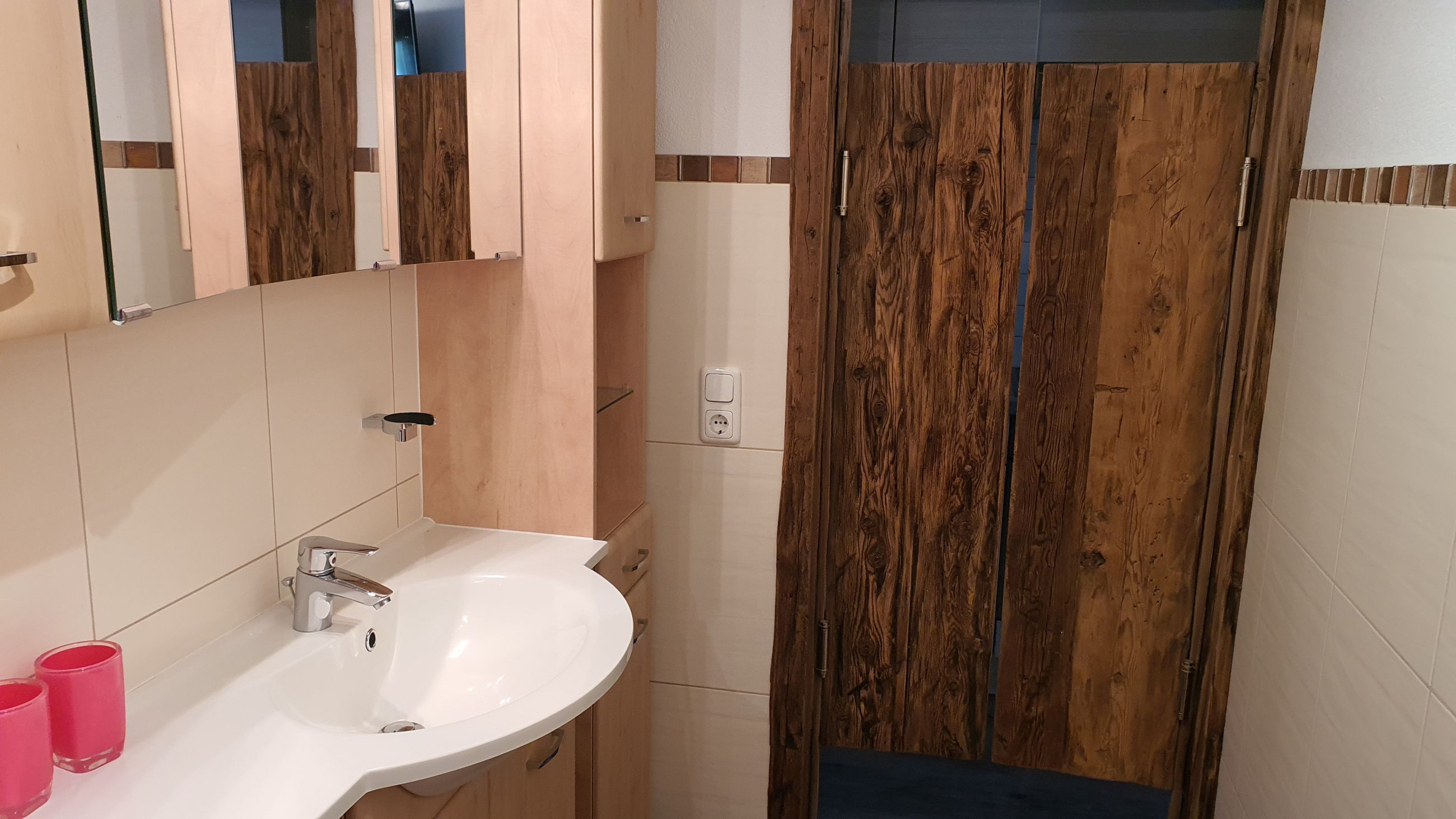 Une salle de bain avec un lavabo blanc, un miroir et des portes en bois.
