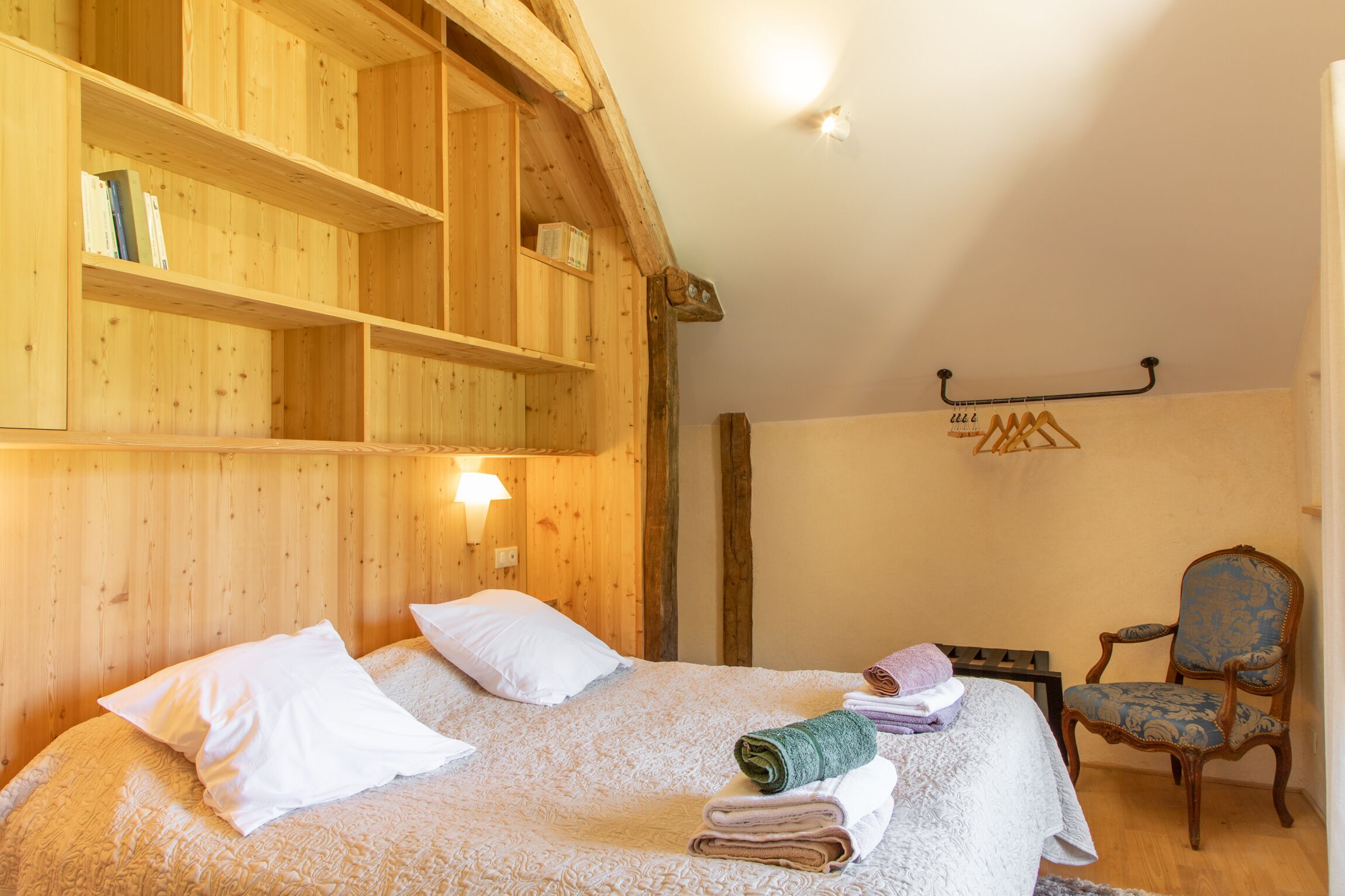 Ein Zimmer aus Holz mit einem Bett, einem Sessel und einem an der Wand befestigten Regal.