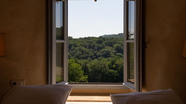 A room with a large window offering a view of a forested hill. - La Grange Milou (Beynac-et-Cazenac)