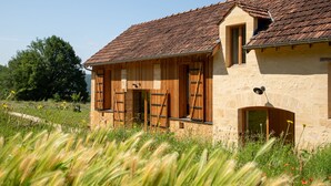 A rustic stone building with wooden shutters, a sloped roof, and a small window. - La Grange Milou (Beynac-et-Cazenac)