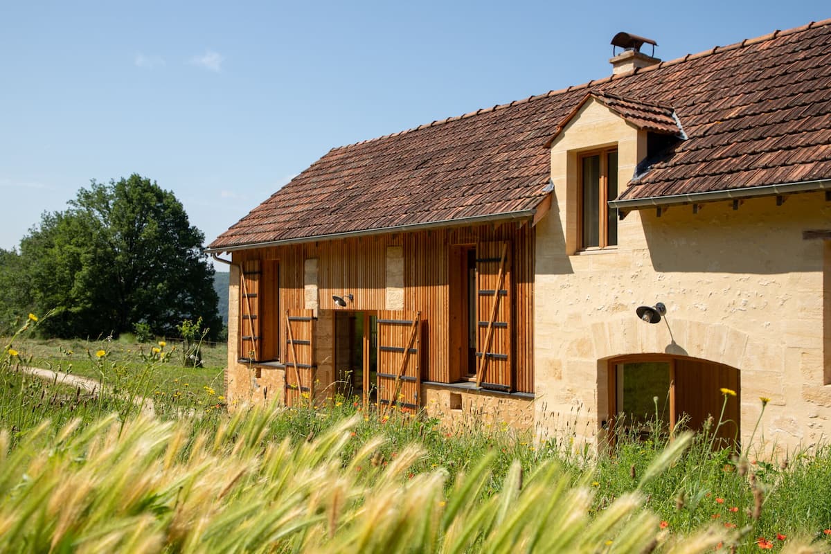 Un bâtiment rustique en pierre, doté de volets en bois, d’un toit en pente et d’une petite fenêtre.