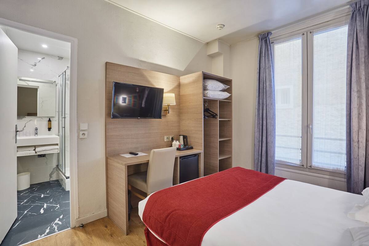 Ein Hotelzimmer mit Bett, Schreibtisch, Fernseher, Spiegel und einem Fenster mit Vorhängen.