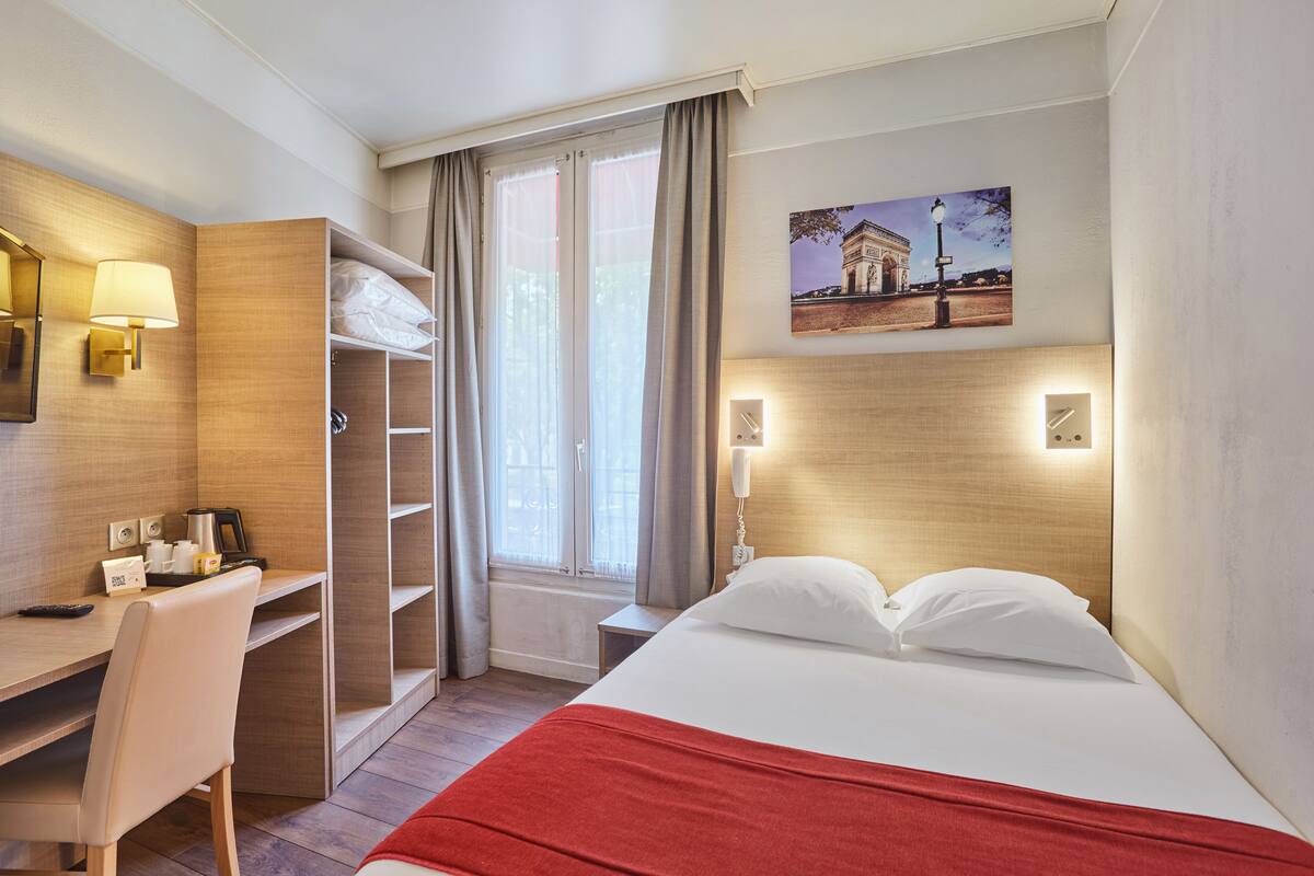 Ein Hotelzimmer mit Bett, Schreibtisch, Stuhl, Kleiderschrank und einem Fenster mit Vorhängen.