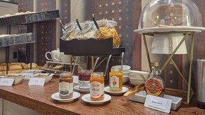 Un buffet de petit-déjeuner avec des récipients étiquetés contenant différentes sortes de tartinades, un bocal en verre de sirop d’érable et un panneau indiquant la présence de crêpes.