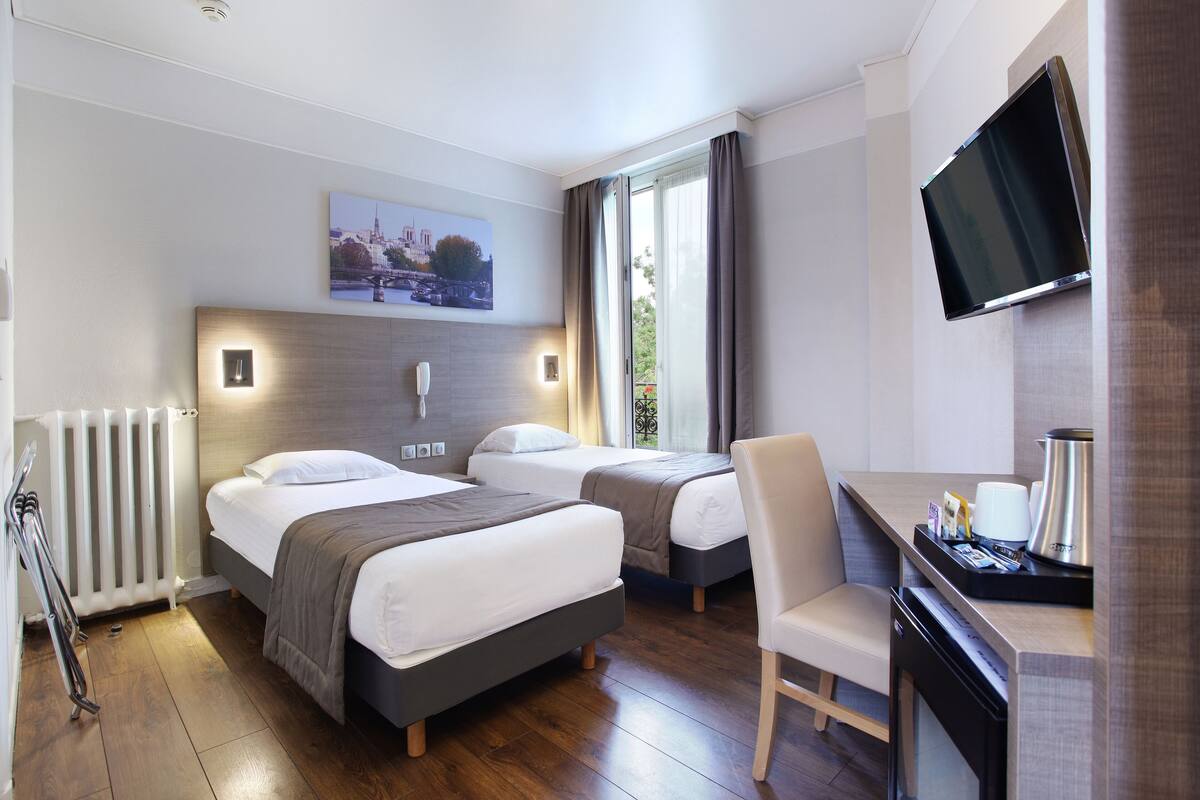 Ein Hotelzimmer mit zwei Betten, einem Schreibtisch, einer Kaffeemaschine, einem Fernseher und Blick ins Freie.