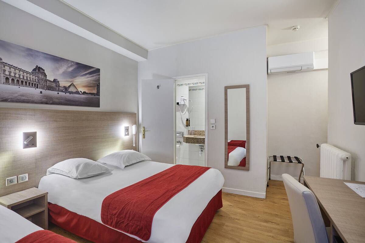 Ein Hotelzimmer mit Bett, Schreibtisch, Stuhl, Duschbereich und einem Bild an der Wand.