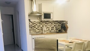 A modern kitchen with a microwave, stove, and tiled backsplash. There is a dining area with a table and chairs. - Olas de Lobos (Corralejo)
