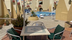 An outdoor seating area with a table and chairs, a pool in the background, and potted plants. - A&V Mareverde Costa Adeje Luxury Poolfront Apartment (Costa Adeje)