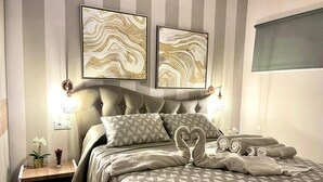 A bedroom with a tufted headboard, a patterned bedspread, and two abstract wall art pieces. - A&V Mareverde Costa Adeje Luxury Poolfront Apartment (Costa Adeje)