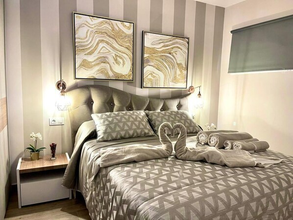 A bedroom with a tufted headboard, a patterned bedspread, and two abstract wall art pieces.