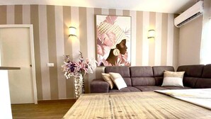 A living room with a sofa, a rug, a wall-mounted artwork, and a vase with flowers. - A&V Mareverde Costa Adeje Luxury Poolfront Apartment (Costa Adeje)