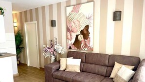 A living room with a brown sectional sofa, a large abstract painting, and a potted plant. - A&V Mareverde Costa Adeje Luxury Poolfront Apartment (Costa Adeje)