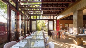 A covered outdoor dining area with tables set for a meal, a brick wall, and a view of the outdoors. - Mira Maré Praia Hotel (Guarujá)
