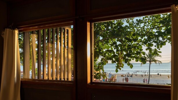 A room with a view of a beach through a window with vertical blinds. - Mira Maré Praia Hotel (Guarujá)