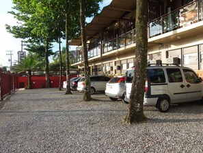 A parking area with several cars, a building with balconies, and trees. - Mira Maré Praia Hotel (Guarujá)
