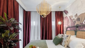 A hotel room with a bed, a dining table with breakfast, red and white curtains, a hanging light fixture, and a large plant. - Birds of Paradise (Bucharest)
