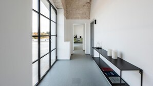 Un pasillo moderno con ventanas amplias, techo de hormigón y una mesa de recepción con tarjetas informativas.