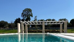 Una piscina azul cristalina con una estructura de pérgola blanca al fondo.
