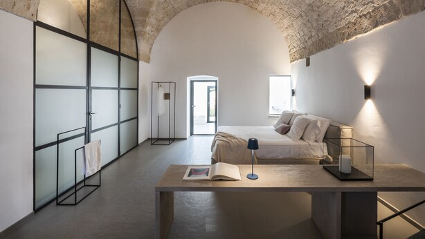 Un dormitorio con techo de piedra, una cama con almohadas, una mesita de noche con lámpara y un armario con puertas correderas.