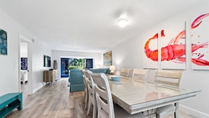 A modern dining area with a glass-top table, white chairs, and a teal bench. - Siesta Dunes 6-102, Peaceful Garden View Unit, 2br/2ba, 1st Floor Condo (Sarasota)