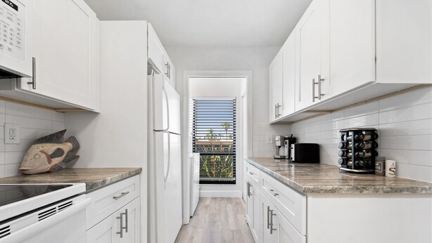 A modern kitchen with white cabinets, a wooden countertop, and a view through a door. - Siesta Dunes 6-102, Peaceful Garden View Unit, 2br/2ba, 1st Floor Condo (Sarasota)