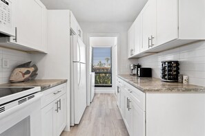 A modern kitchen with white cabinets, a wooden countertop, and a view through a door. - Siesta Dunes 6-102, Peaceful Garden View Unit, 2br/2ba, 1st Floor Condo (Sarasota)