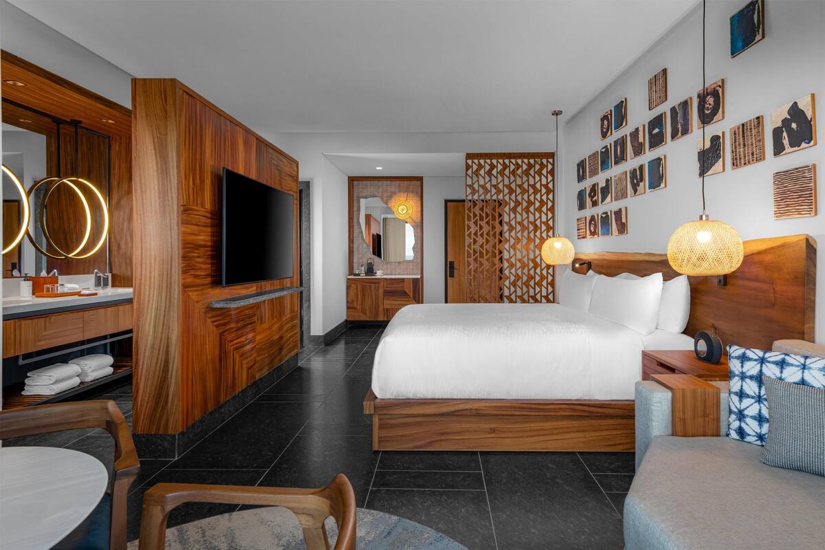 Une chambre d’hôtel moderne dotée d’un grand lit, de meubles en bois, d’un téléviseur à écran plat et d’œuvres d’art accrochées aux murs.