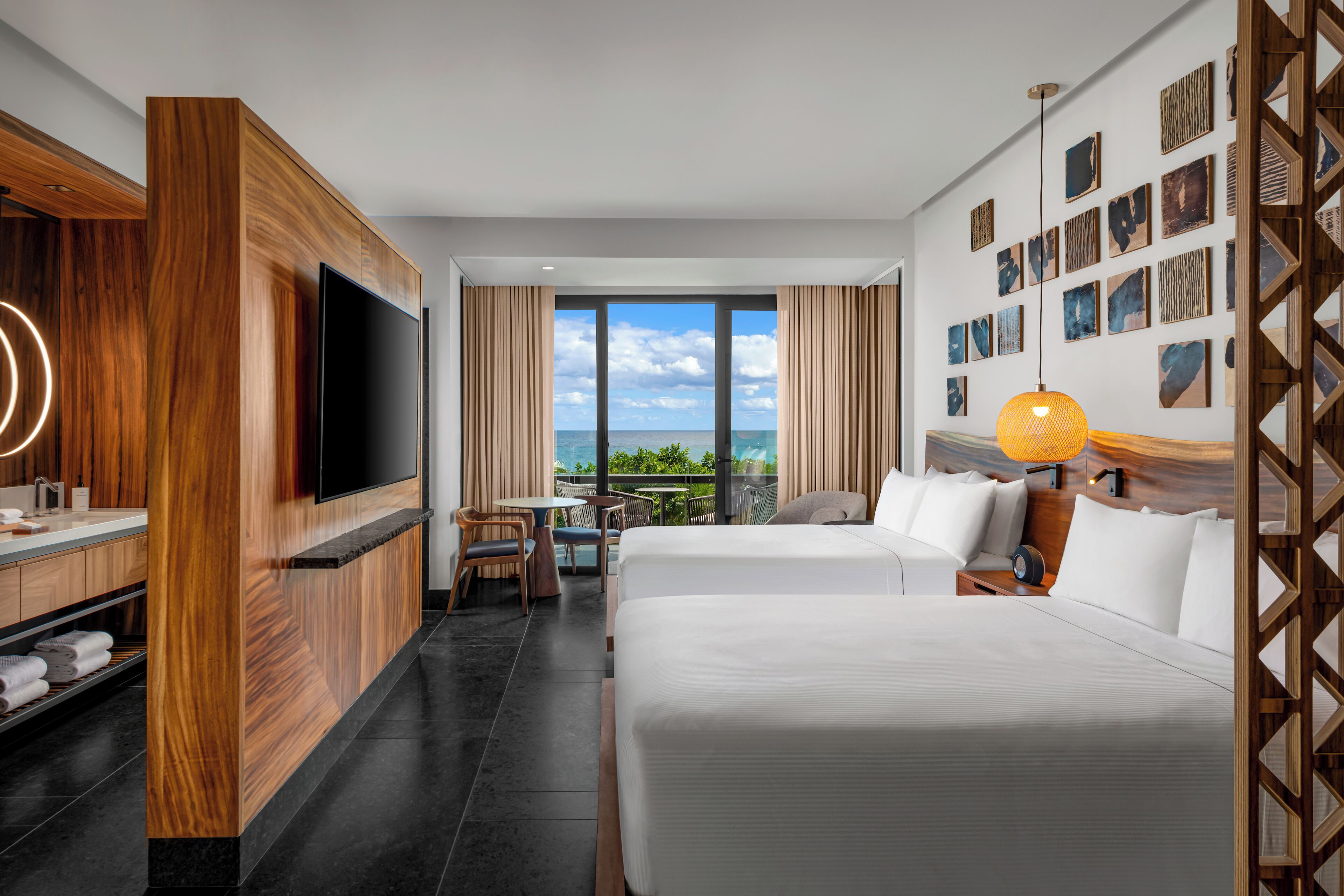 A hotel room with a large bed, a TV, a desk with a chair, and a balcony with a view of the sea.