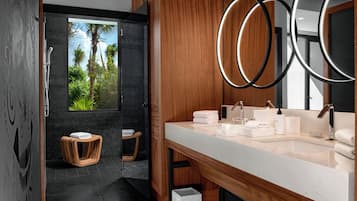 A modern bathroom with a large mirror, wooden cabinets, a marble sink, and a view of palm trees.