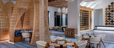 A modern dining area with geometric patterned flooring, wooden tables, white chairs, and woven light fixtures.