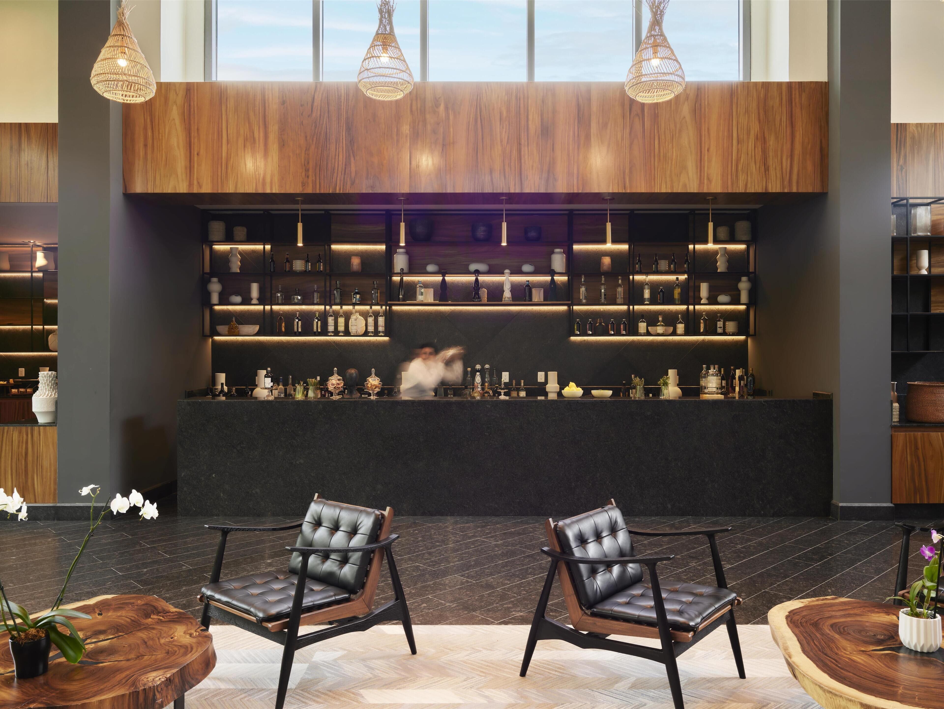 A modern bar area with wooden paneling, shelves of bottles, and two leather chairs.