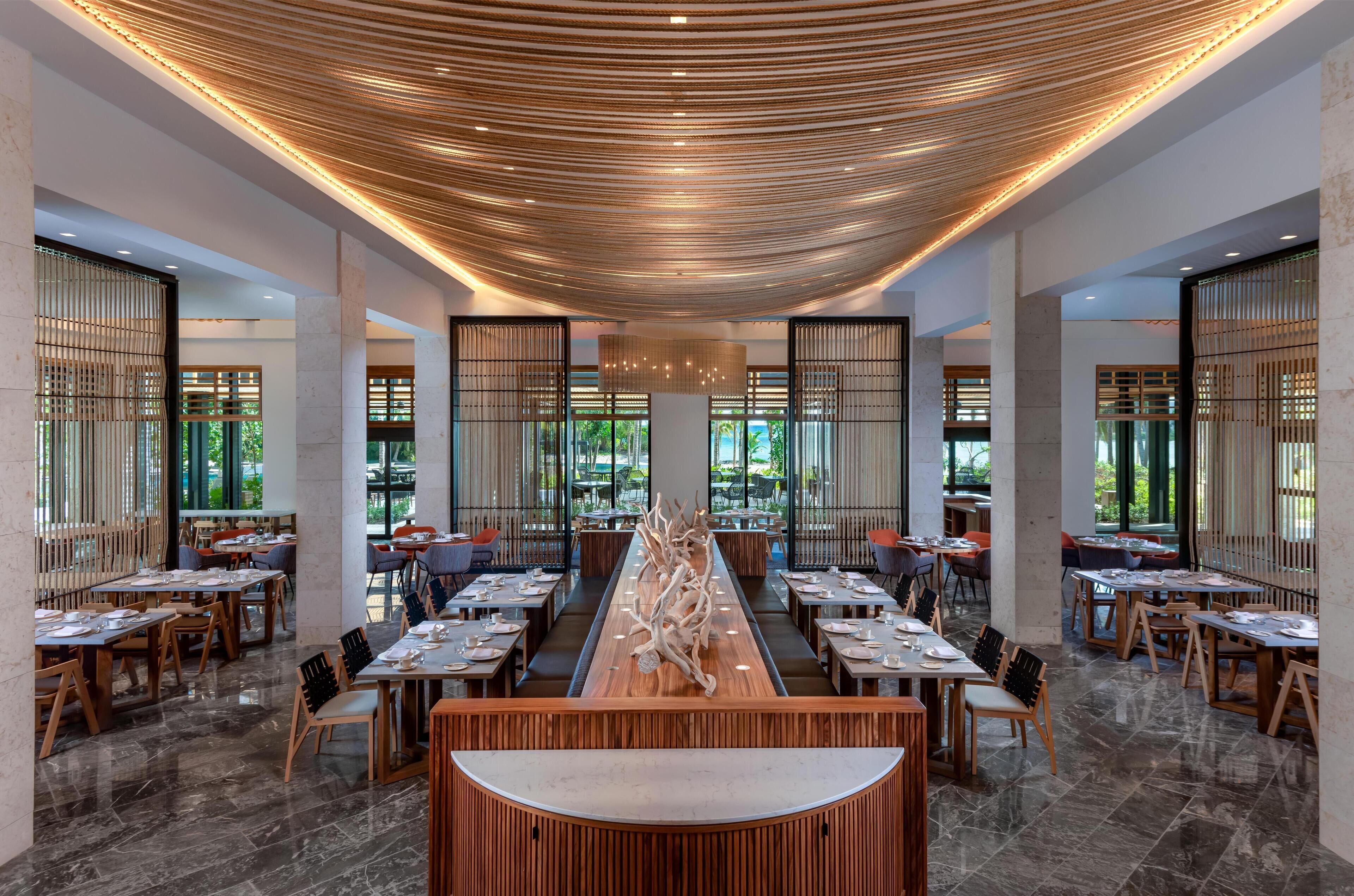 A spacious restaurant with a long wooden table in the center, surrounded by multiple dining tables and chairs.