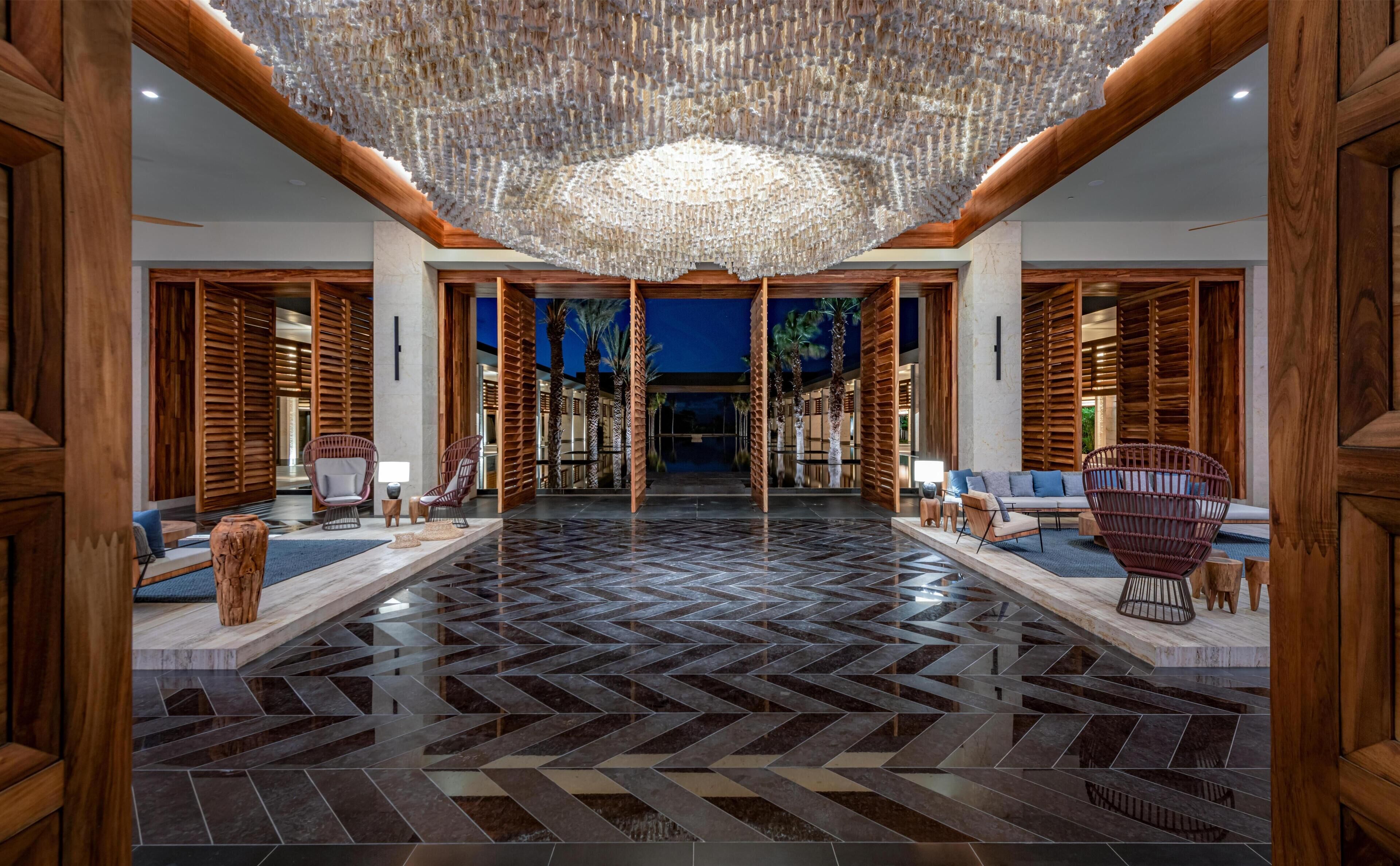 Un hall d’entrée spacieux, doté d’un parquet à motifs en chevrons, de boiseries et d’un lustre central.