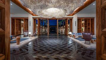 Un hall d’entrée spacieux, doté d’un parquet à motifs en chevrons, de boiseries et d’un lustre central.