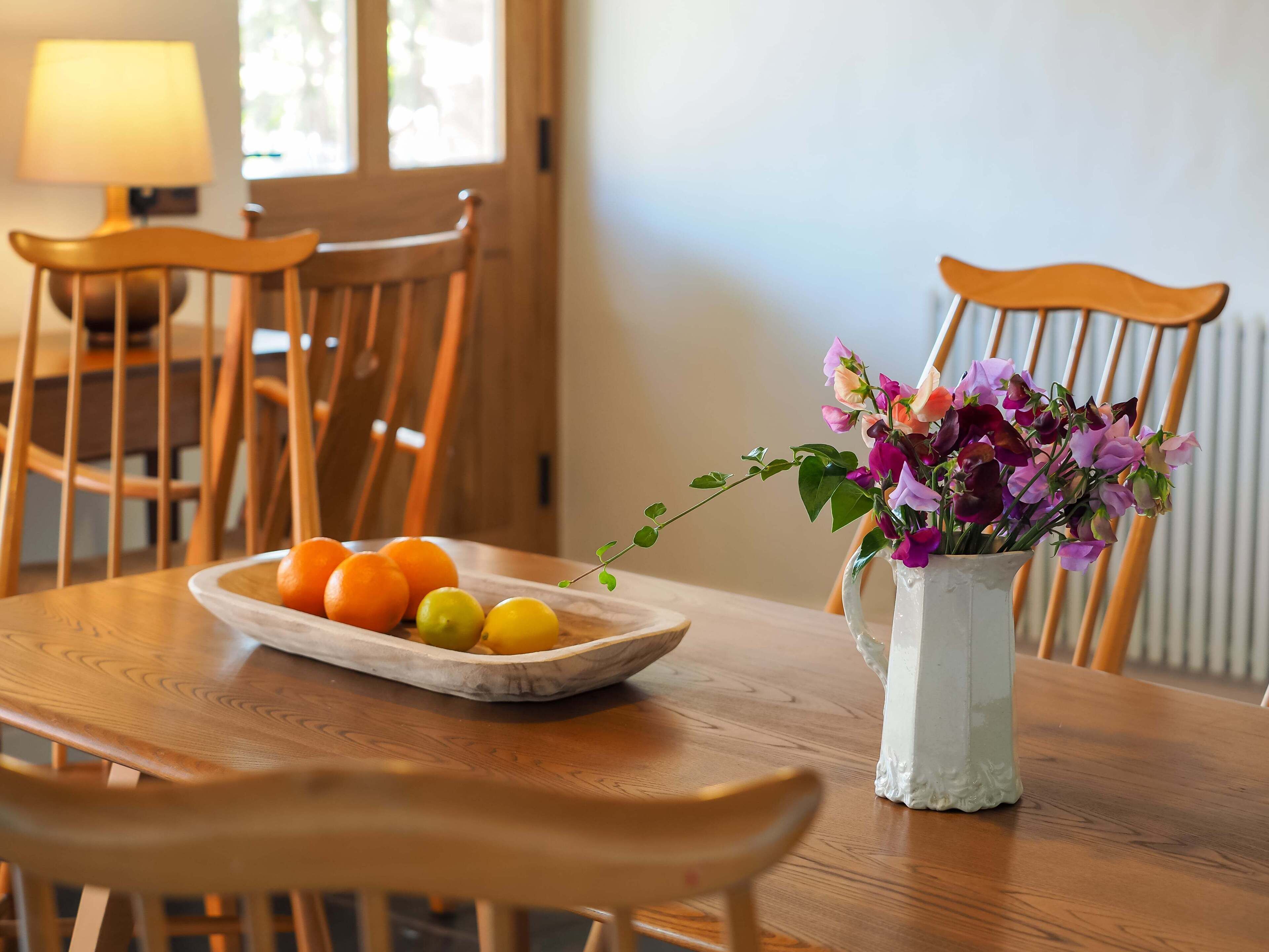A wooden dining table with a plate of fruit and a vase of flowers.