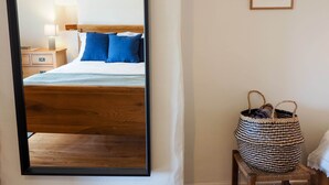 Quarto com cama de madeira, almofadas azuis, mesa de cabeceira com abajur e duas molduras na parede.