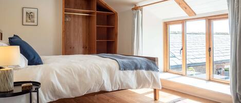 Un dormitorio con cama, armario de madera, ventana con cortinas y vistas al exterior.