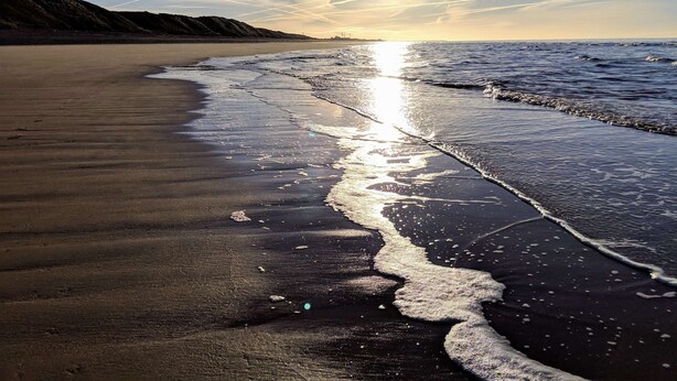 Uma praia com céu claro e luz do sol refletindo na areia molhada.