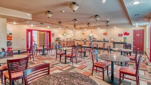 A spacious restaurant with multiple tables and chairs, a kitchen area, and a patterned floor. - Express Inn & Suites (Norman)