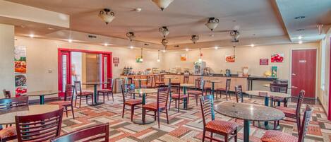Un restaurante espacioso con varias mesas y sillas, una zona de cocina y un suelo con diseño.