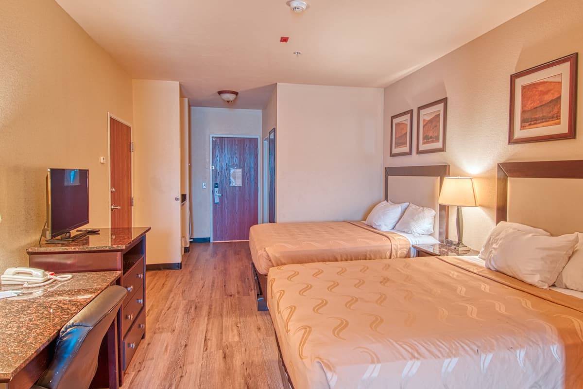 Habitación de hotel con dos camas, un escritorio con teléfono, televisor y una puerta que da a otra habitación.