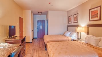 A hotel room with two beds, a desk with a telephone, a television, and a door leading to another room.