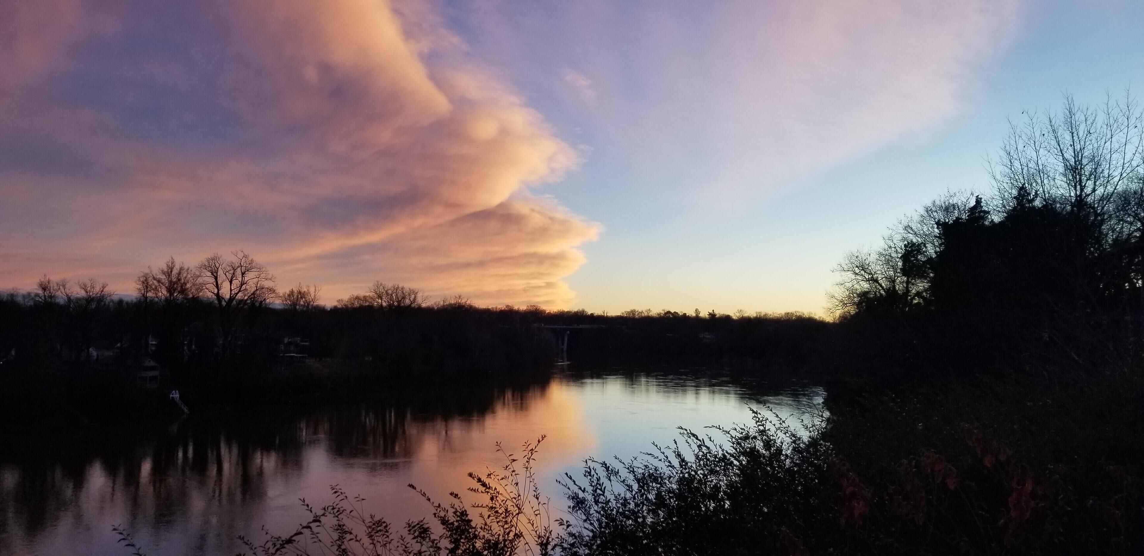 Un lago tranquilo con un puente a lo lejos y un cielo al atardecer.