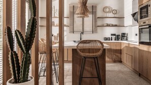 A modern kitchen with wooden cabinets, a central island with a woven chair, and a hanging light fixture. - Sentiero Iconic Villa, a Serene Retreat (Zakynthos)