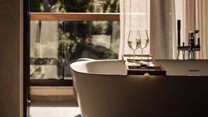 A modern bathroom with a freestanding bathtub, a glass of white wine, and a view of a garden through a large window. - Sentiero Iconic Villa, a Serene Retreat (Zakynthos)