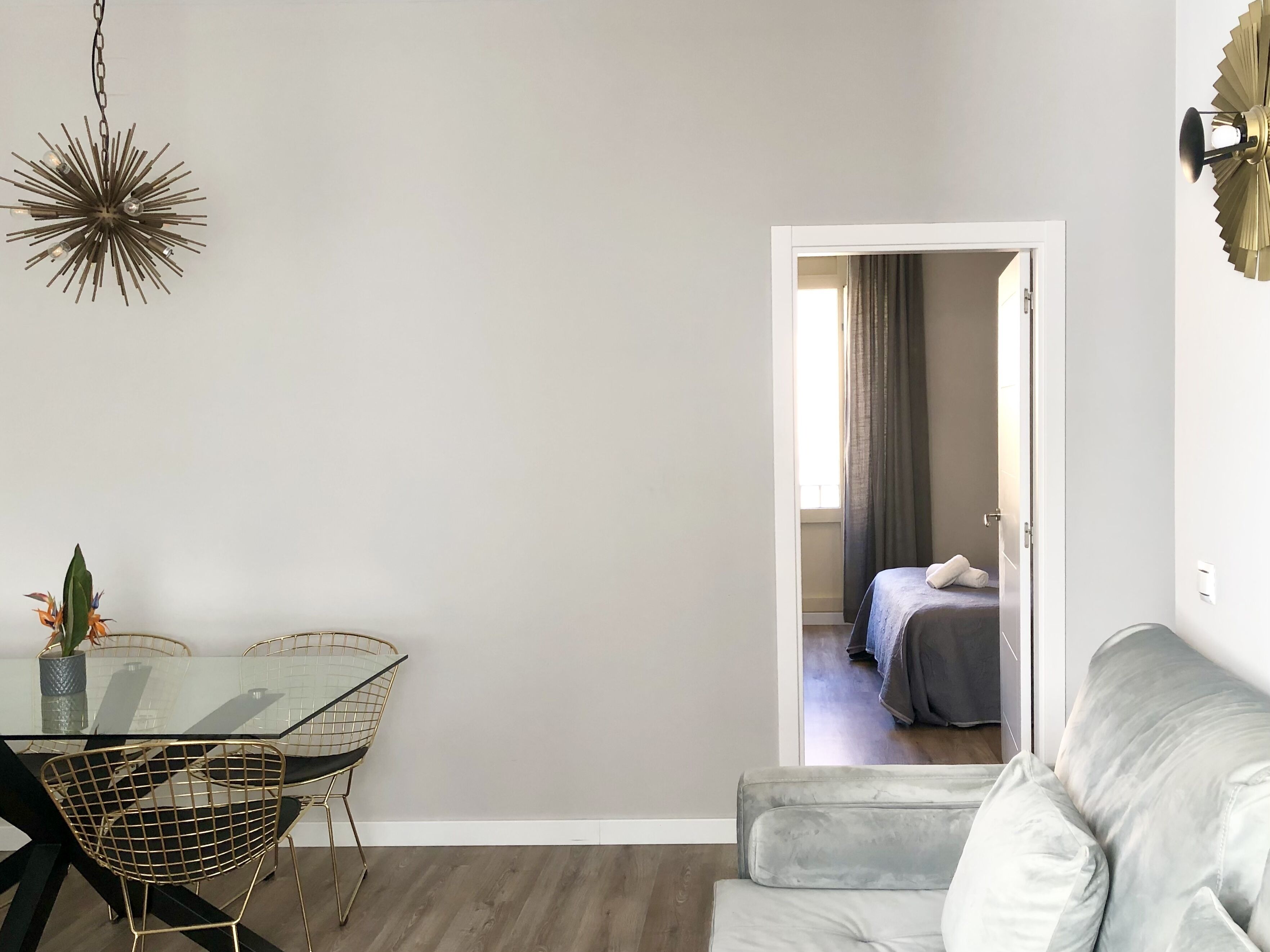 Una sala moderna con una mesa de comedor de cristal, un sofá y una cama en la habitación contigua.